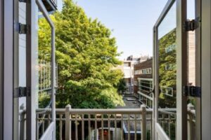 Uitzicht vanaf een open balkon aan de Paulus Potterstraat op een binnentuin met groene bomen en omliggende gebouwen.